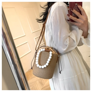 Detail of woven straw bucket bag featuring large white bead handle and drawstring inner lining