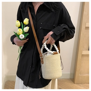 Close-up of woven bucket bag featuring white beaded handle and brown leather strap