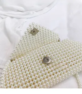 Detailed macro view of the silver magnetic clasp on a white pearl beaded handbag