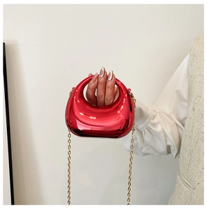 Mini mirror red half-moon handbag with gold chain strap held by hand in detail