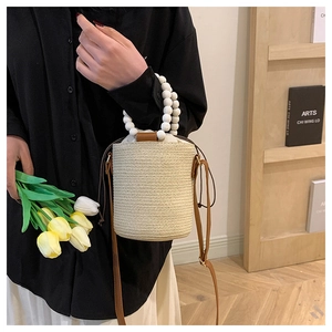 Detail of beige woven bucket bag with white wooden bead handle and drawstring closure