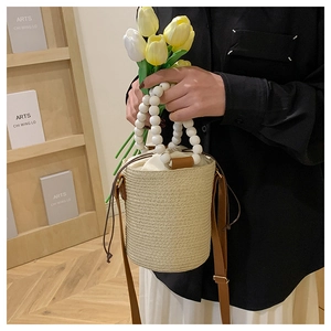 Detail of woven bucket bag featuring white beaded handle and drawstring closure