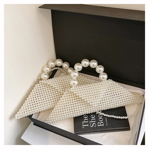 Detail view of woven pearl triangle handbag with large handle inside a black gift box