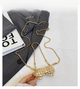 Macro detail of peanut shaped gold metal mini bag with textured shell surface and bead chain
