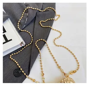 Detail of the golden metal ball chain strap with textured orb ornament on a grey blazer