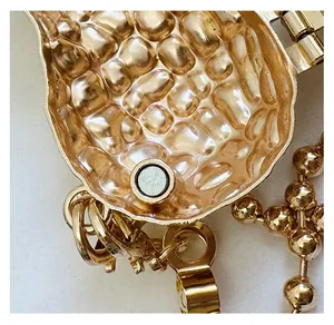 Detail of gold magnetic buckle with hammered texture and lobster clasp on bag