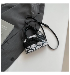 Vista piatta di una borsa a guscio pitonata su un blazer grigio con accessori moda
