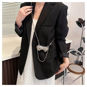 Detail of silver rhinestone bow crossbody bag with metallic chain on a model outfit