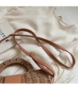 Detail of woven straw handbag featuring adjustable brown leather strap and gold buckle