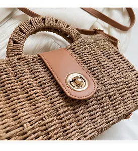 Close-up of a straw beach bag with brown leather flap and golden twist-lock buckle