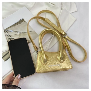 Mini gold trapezoid handbag with textured finish next to a phone for size scale