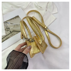 Detailed close-up of metallic gold mini square bag with leather handle and slim strap