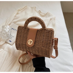 Detail of a brown woven beach bag with leather top handle and gold metal twist lock buckle