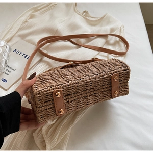 Close-up of woven straw bag bottom with protective gold metal studs and leather strap detail