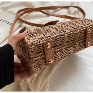 Detail view of woven straw bag bottom with brown leather reinforcement and metal studs