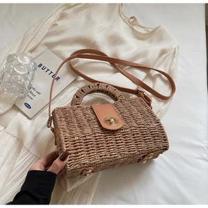 Close-up of woven straw handbag featuring a gold metal twist lock and leather flap detail