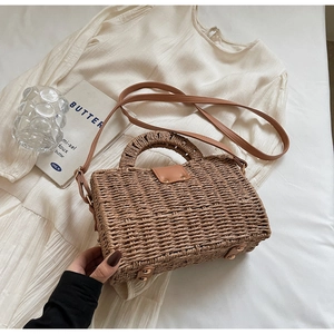 Close-up of natural woven straw handbag with brown leather strap and metal bottom studs