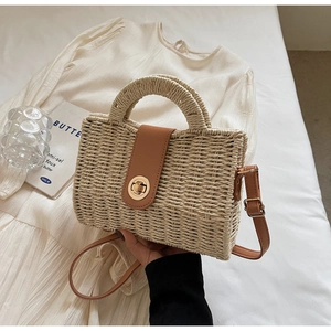 Detail of woven straw handbag with brown leather flap and golden twist-lock closure