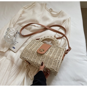 Detailed view of beige woven straw handbag with brown leather flap and gold twist lock