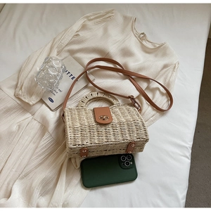 Close-up of woven straw handbag with brown leather trim and golden twist lock