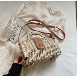 Close-up of woven beach bag with golden lock and brown leather strap on white dress