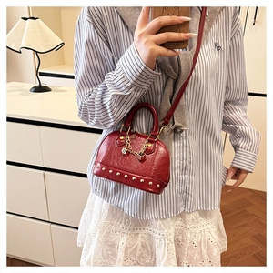 Detail of red shell handbag featuring golden rivets, dice charm, and leather strap