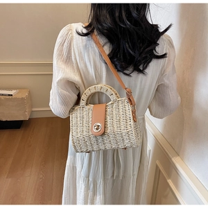 Detail of woven straw handbag with brown leather strap worn by a model in a minimal room