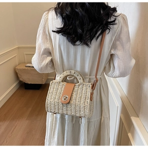 Detail showing hand-woven straw crossbody bag with brown leather strap and metal twist lock
