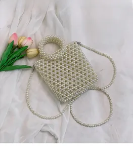 Close-up of white faux pearl woven handbag with fixed top handle and long pearl chain strap