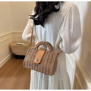Detail of woven straw handbag featuring a gold twist lock and leather shoulder strap