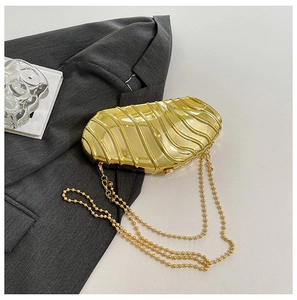 Detail of golden acrylic clutch featuring wave texture and beaded metal chain strap