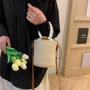 Woven straw bucket bag with white beaded handle and drawstring closure for summer fashion