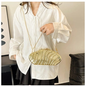 Detail of a golden hardshell evening bag featuring a wavy texture and beaded chain strap