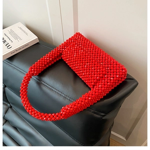 Detail of red acrylic beaded handbag with woven handle on black leather background