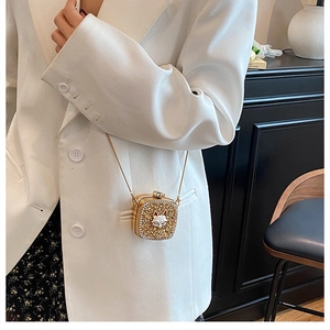 Detailed view of mini gold rhinestone clutch with cat charm on a white blazer outfit