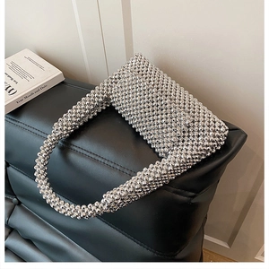 Detailed view of shiny silver acrylic beaded woven handbag on a sleek leather seat