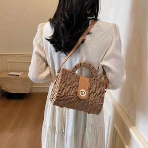 Woven straw handbag with leather strap and metal buckle, shown on a female model in a dress