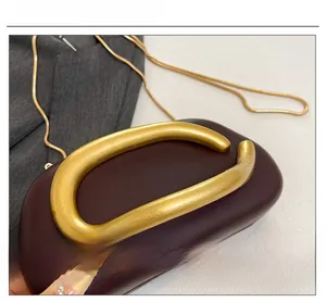 Detail of burgundy leather clutch with gold C-shaped buckle and snake chain strap