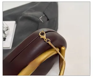 Detailed close-up of golden metal lobster clasp and chain on dark brown leather bag