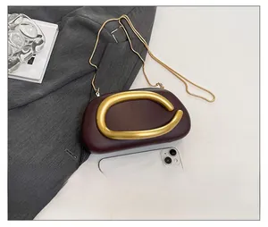 Macro view of burgundy evening clutch bag with gold C-handle and fine snake chain