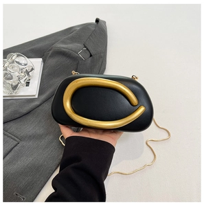 Detail of black leather clutch bag with oversized gold metal buckle and chain strap