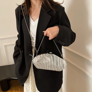 Silver metallic shell clutch bag with wavy texture and chain strap on a model