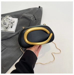 Detail of black hard shell shell bag featuring a large gold C-shaped metal handle and chain