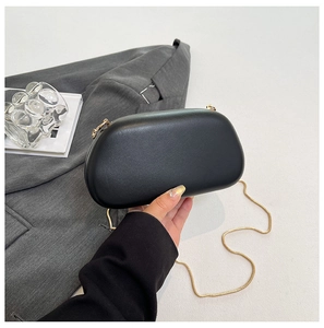 Detail of elegant black hard-shell evening clutch with fine golden metal chain strap