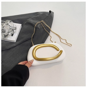 Macro detail of white pebble-shaped evening clutch with gold metal handle and chain