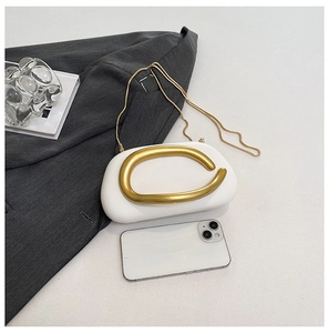 Mini white pebble clutch with sculptural gold handle and chain, shown next to a smartphone