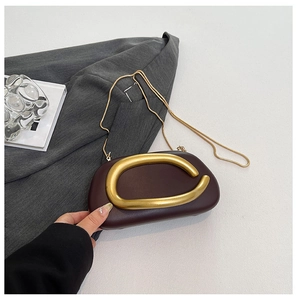 Detail view of burgundy leather clutch featuring a gold C-clasp and metallic chain strap