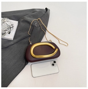 Close-up of a burgundy mini shell bag with a large gold circular metal buckle and chain