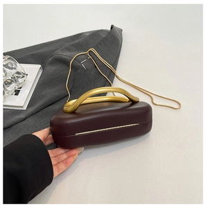 Detail of burgundy clutch bag with fluid gold metal handle and long chain strap