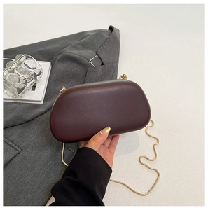 Handheld dark red egg-shaped shell bag with elegant gold snake chain over a grey blazer